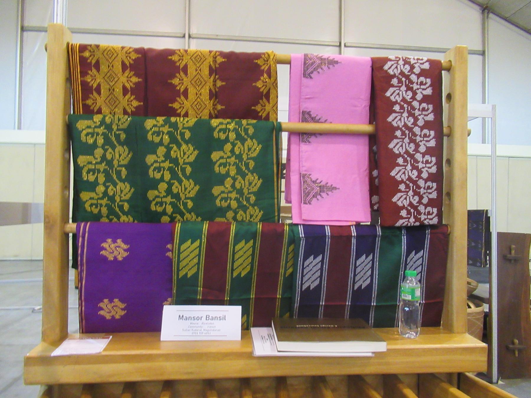 'Likha' (Exhibit) 08 - a wooden display with a variety of different colored towels